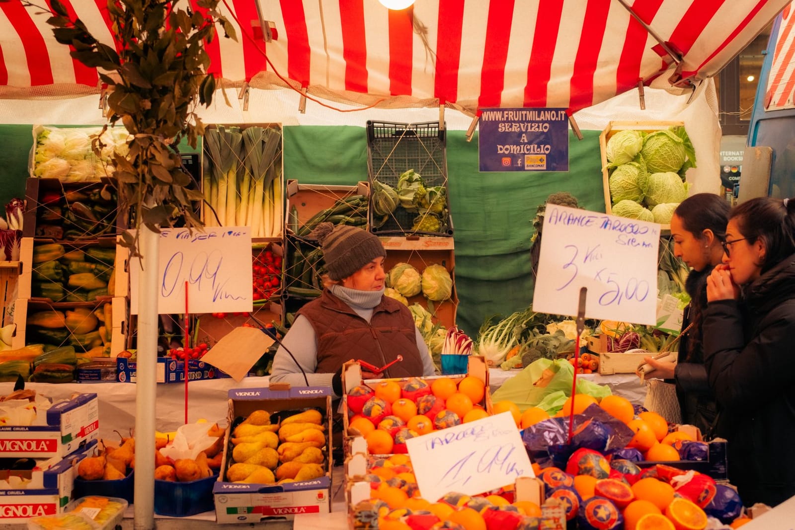 Un banco di frutta e verdura al mercato, con i cartelli dei prezzi scritti a mano