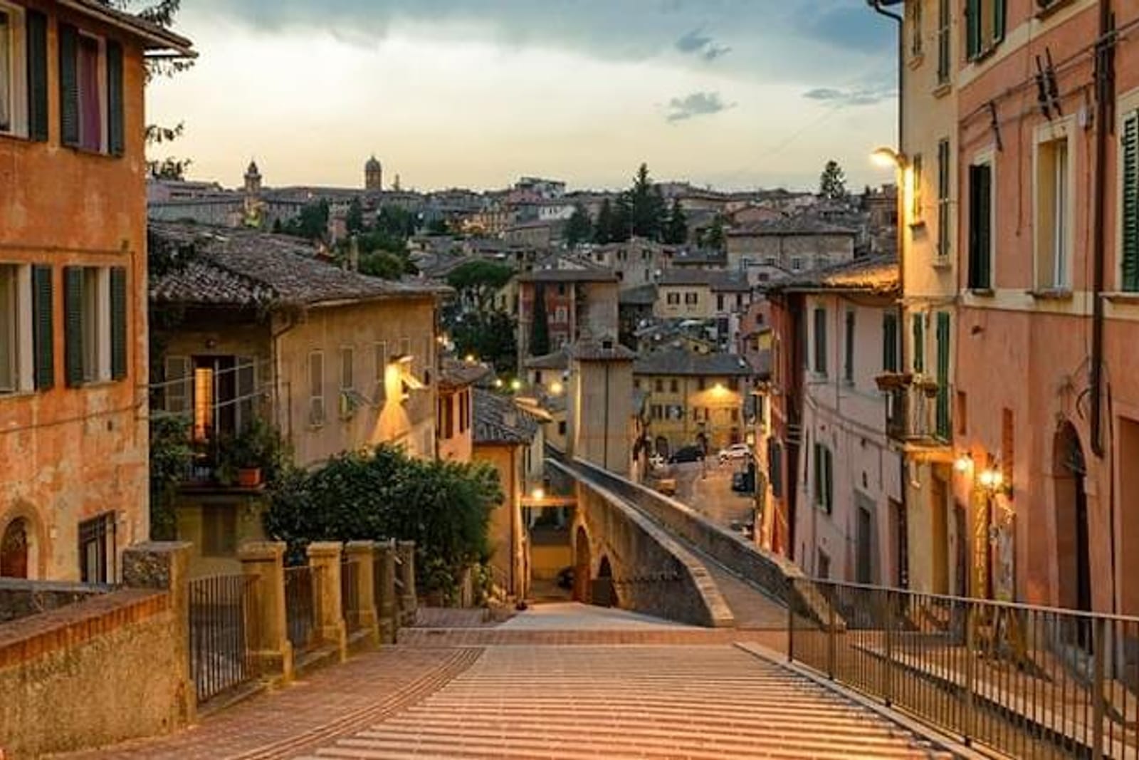 A sloping lane in the centre of Perugia at dusk, stone houses and lit street lamps