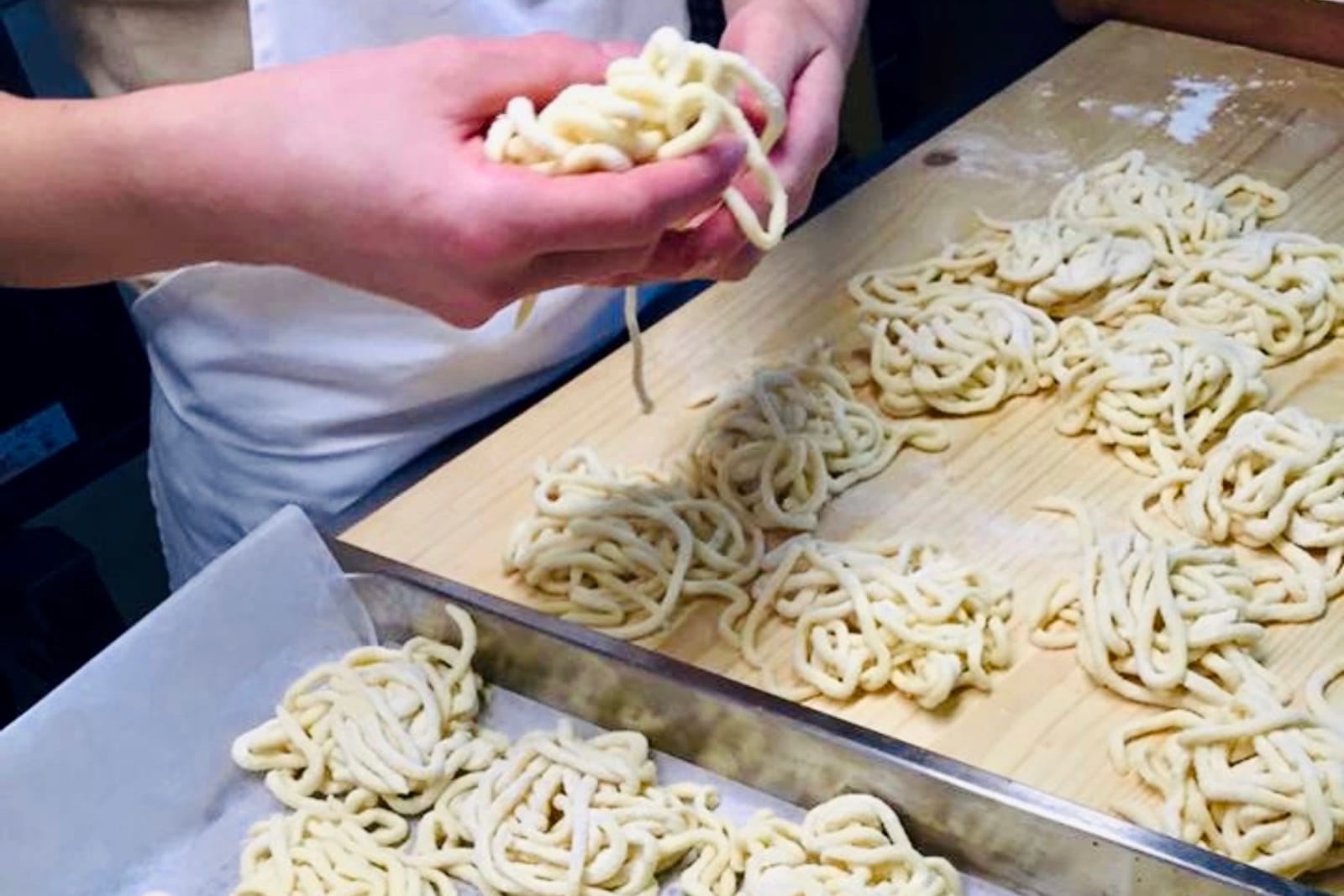 Two hands rolling pici by hand on a floured tray