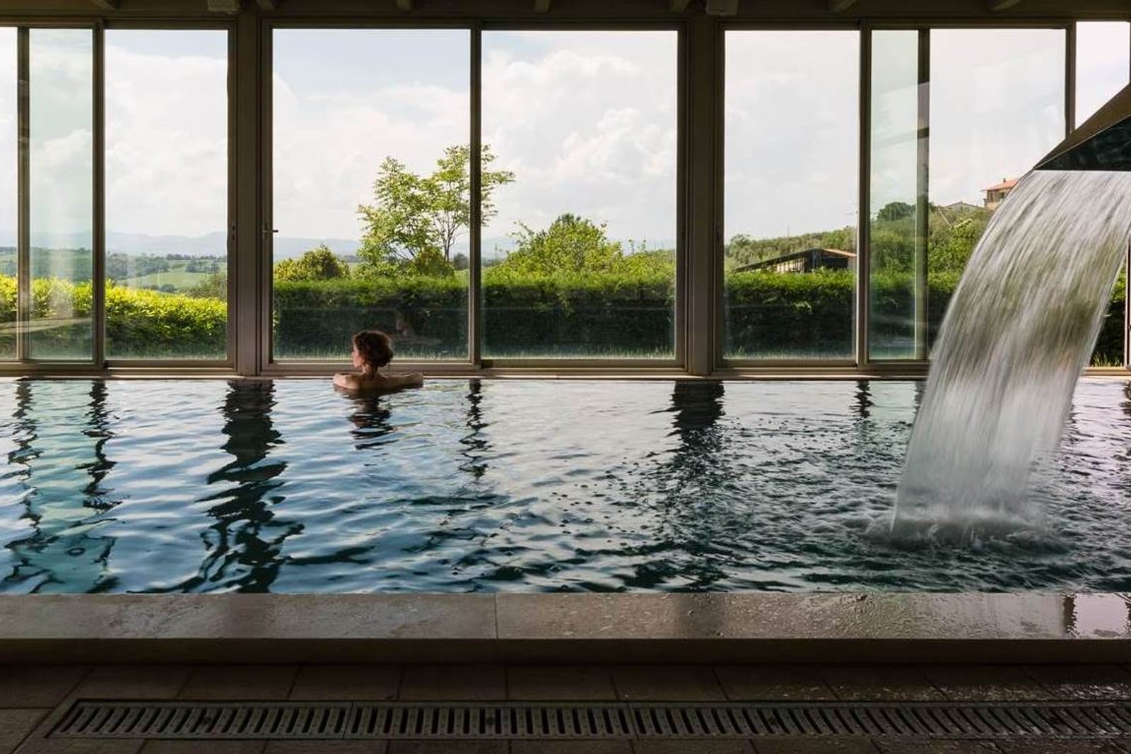 The water cascade in the indoor pool, someone swimming under the glazed wall