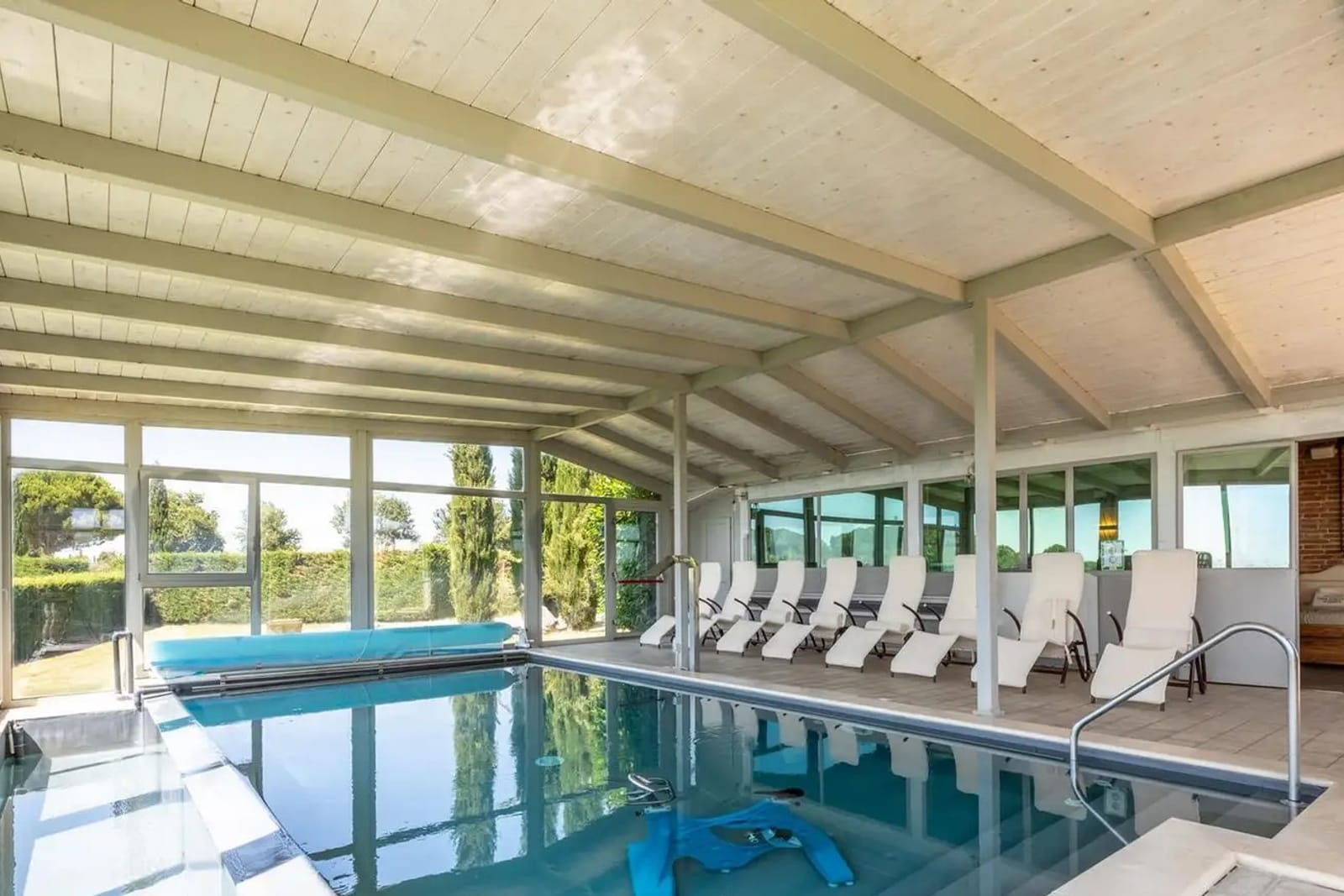Das Hallenbad mit leeren Liegen und der Glasfront zur Landschaft