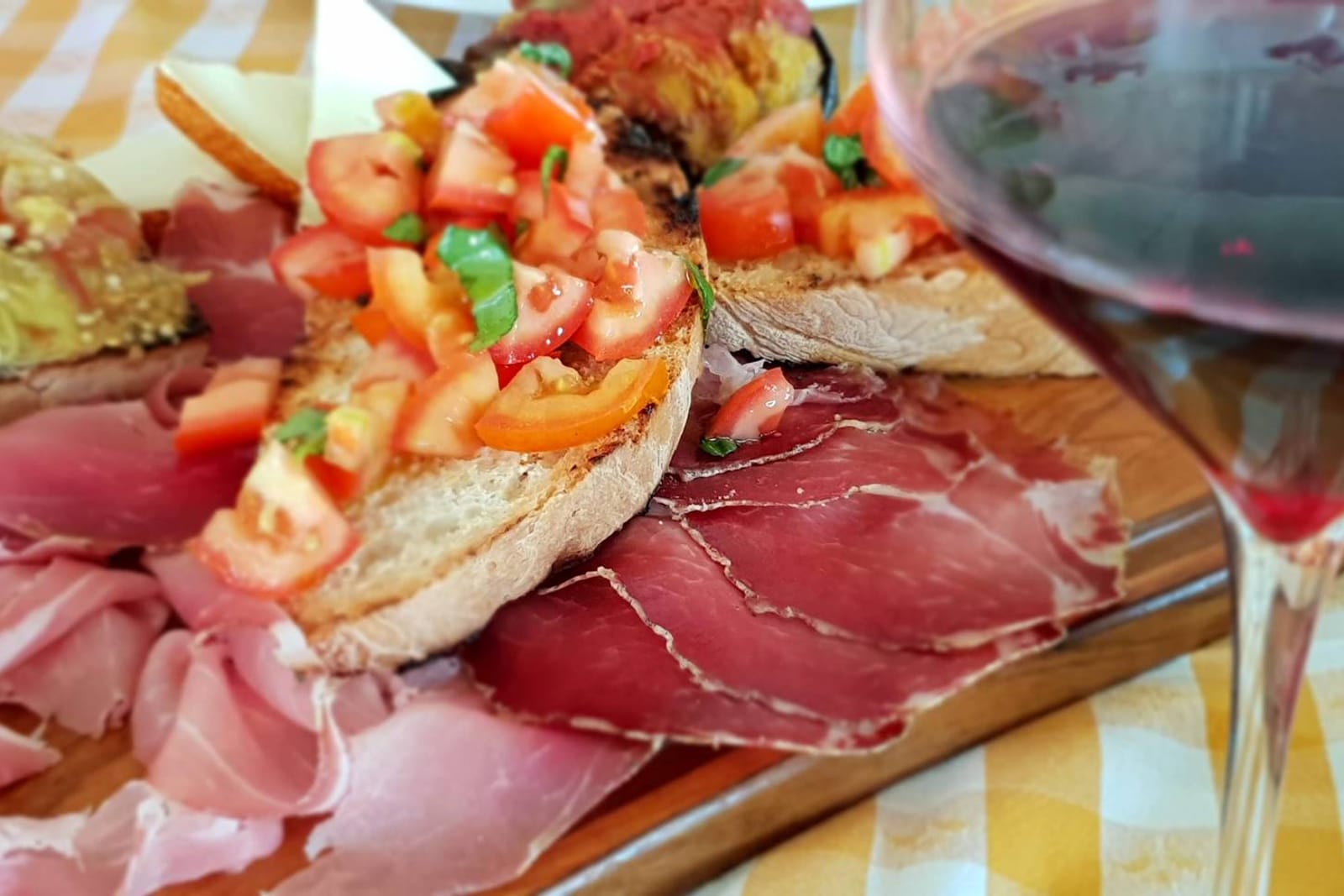 A board of cured meats and crostini with a glass of red wine beside it