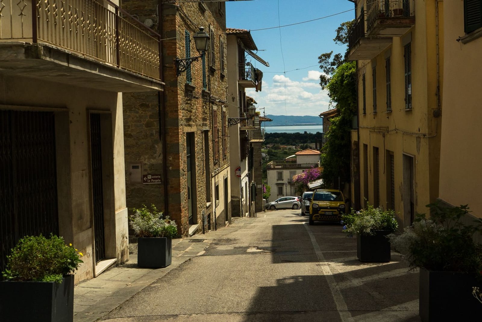 A street running downhill between the stone houses of Tuoro sul Trasimeno, opening onto the lake